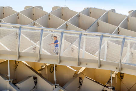 Small boy running on walkways of Setas de Sevilla - wooden construction with walkways on the roof in...
