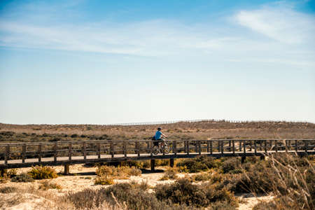 A father riding a bicycle with his baby boy on wooden boardwalks of Alvor, Algarve, Portugalの写真素材