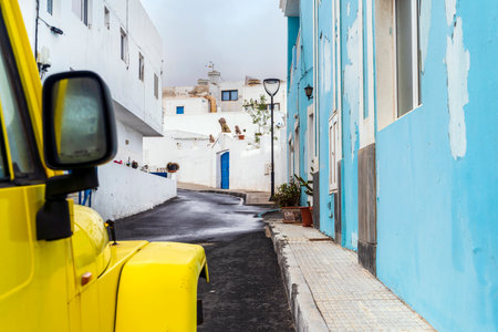 Yellow 4-wheel drive car on narrow street with white and blue buildings in Corralejo, Lanzarote, Canary Islands, Spainの写真素材
