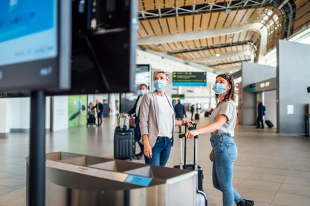 Two traveling women wearing protective masks discussing by flight information board at the Faro airportの写真素材