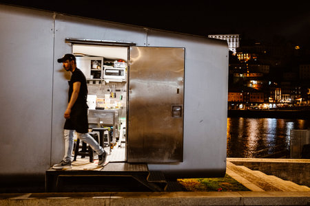 April 17, 2023 - Porto, Portugal: A worker leaving the kitchen in food stall by the river at night