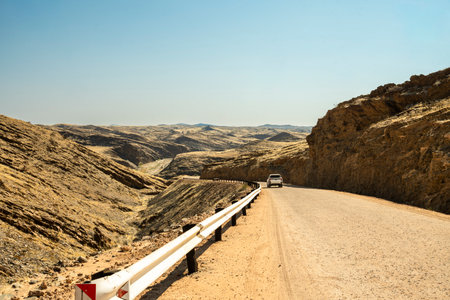 A scenic road running through Namib-Naukluft National Park in Namibia, surrounded by vast desert landscapes, dunes, and mountains under a clear blue sky. The image captures the beauty and solitude of the Namib Desertの写真素材