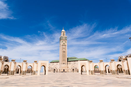 Hassan II Mosque, Casablanca, Morocco â The majestic Hassan II Mosque stands on the Atlantic coast in Casablanca, Morocco, under a bright blue sky. Its tall minaret, ornate arches, and intricate Moroccan architectural details reflect in the ocean below, creating a serene and impressive view of one of the largest mosques in the world.の写真素材