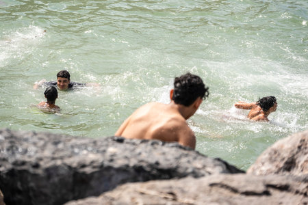 Rabat, Morocco â April 17, 2025: Group of boys swimming and playing in the Atlantic Ocean near rocky shores during a warm summer afternoon. The image captures a joyful and authentic moment of local youth enjoying the sea and sunshine in the Moroccan capital.の写真素材