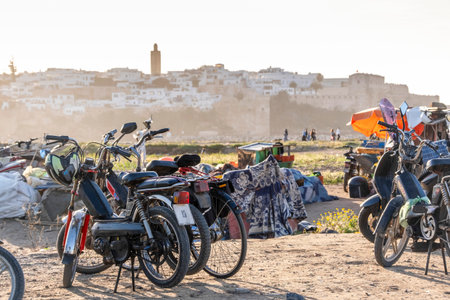 Rabat, Morocco â Parked motorbikes and scooters near the beach with the historic Kasbah of the Udayas and the old medina visible in the background during sunset. The warm golden light highlights the urban coastal life and daily atmosphere of Morocco's capital city, blending modern mobility with traditional architecture.の写真素材