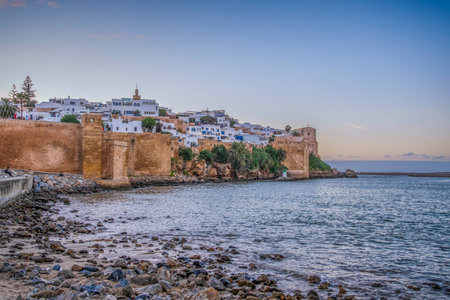Rabat, Morocco â Scenic view of the Kasbah of the Udayas and the Bouregreg River at sunset. The golden light illuminates the historic fortress walls and whitewashed houses overlooking the calm water. A peaceful coastal scene that captures the beauty and heritage of Morocco's capital city.の写真素材