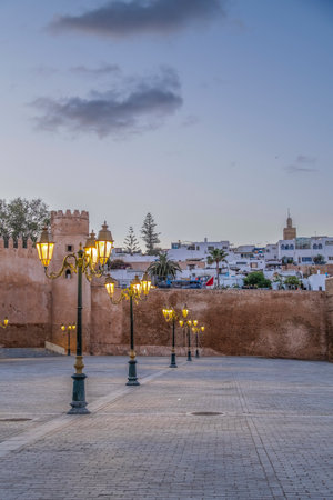 Rabat, Morocco â Evening view of the old medina walls and traditional street lamps illuminated at dusk. The scene captures the peaceful ambiance of the historic area with warm lights reflecting on the stone pavement and the city's white buildings in the background. A serene atmosphere showcasing Moroccan architecture and heritage in the capital cityの写真素材