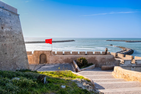 Rabat, Morocco â Scenic view of the historic Kasbah of the Udayas overlooking the Atlantic Ocean. The Moroccan flag waves above the ancient fortress walls near the sea, with stone pathways and blue water under a clear sky. A peaceful and picturesque scene showcasing Moroccan heritage and coastal beauty.の写真素材