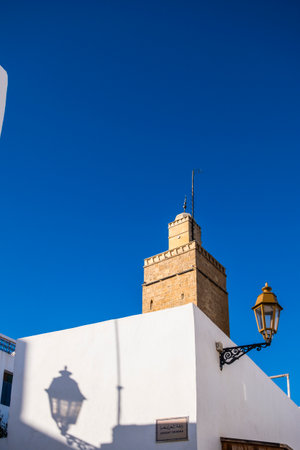 Rabat, Morocco â A quiet narrow alley in the historic medina of Rabat, lined with whitewashed buildings, traditional wooden doors, and decorative street lamps. The cobblestone street leads toward small local shops displaying colorful fabrics, creating an authentic atmosphere that reflects Moroccan architecture and daily life in the old city.の写真素材