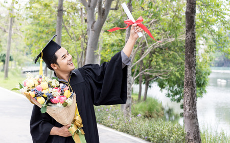 happy graduate showing certificated in hand with in the gardenの写真素材
