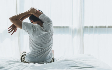 Back of view man wake up and stretching on bed in bedroom in the morning.at home in holiday.の写真素材