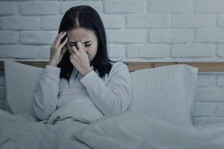 Asian woman sitting and sad on bed with hand touching his head sitting on bed.color toneの写真素材