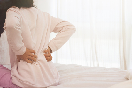 Asian woman back pain and sit on bed in bedroom in the morning.color toneの写真素材