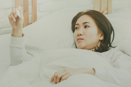 Asian woman use a thermometer to detect fever in bedroom.の写真素材