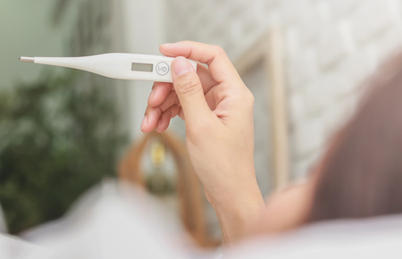 Asian woman use a thermometer to detect fever in bedroom.の写真素材