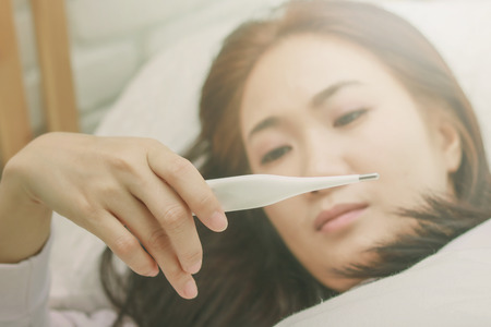 Asian woman use a thermometer to detect fever in bedroom.
