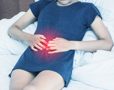 Beautiful Attractive Asian woman wearing white shirt sitting on bed have a bladder pain or uti pain after wake up in the morning feeling so illness,Healthcare Concept.color toneの写真素材