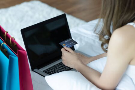 Asian woman paying online. Shopper shopping online with credit card and laptop on bed in home.shopping online concept.の写真素材