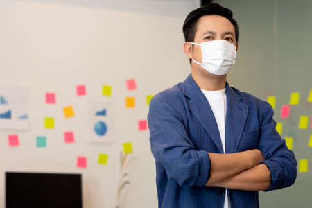 Business asian man stand and wear masks and cross arm in the office.の写真素材