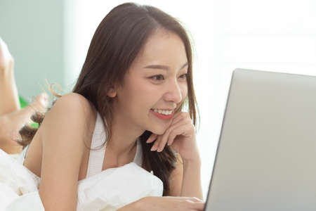 Asian woman working on a laptop sitting on the bed in the house.の写真素材