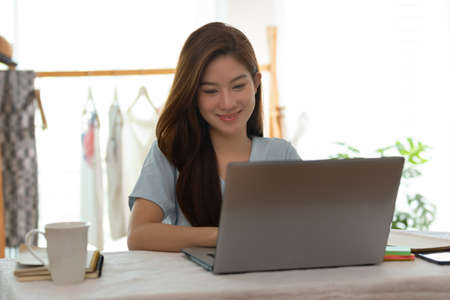 Asian woman working on a laptop sitting on the bed in the house.の写真素材