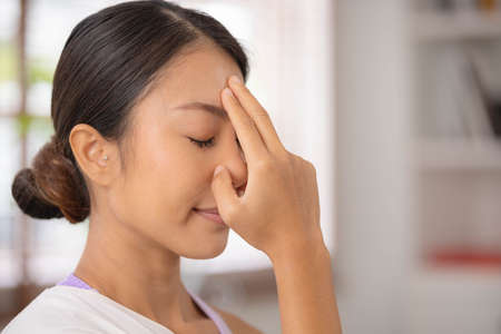 To guide her breath, an Asian lady touches her forehead with her fingers. To get started with yoga...