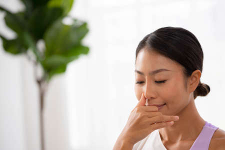 To guide her breath, an Asian lady touches her nostrils with her fingers. To get started with yoga and meditationの写真素材