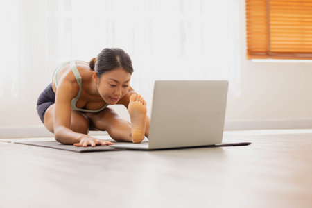 Asian woman relaxes in home. You start studying yoga in the morning by turning on the computer and joining the class.の写真素材