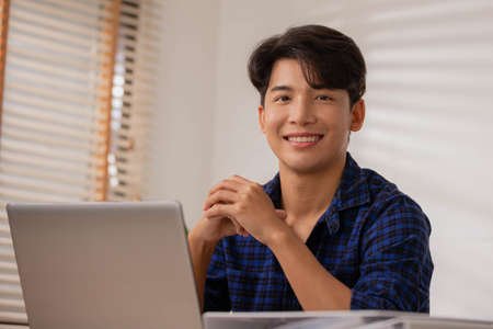 Asian entrepreneur At home, after a long day at the office, I sit and relax on my desk table, smiling and happy.の写真素材