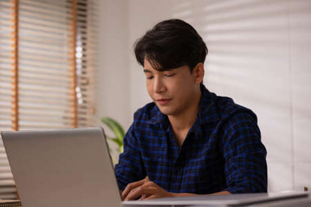 Asian businessman, anxious and exhausted from working online at home on a desk with a laptop.の写真素材
