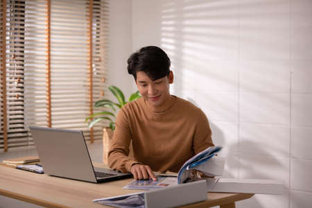 At home, an Asian businessman works on a desk with a laptop, searching for jobs and paperwork.
