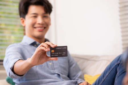 Asian man makes a payment via the internet. On the sofa at home, a shopper shops online using a credit card and a smartphone. The concept of internet shopping.の写真素材