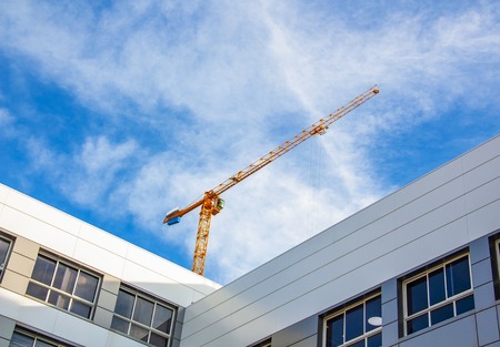 The orange boom of a crane between modern buildingsの写真素材