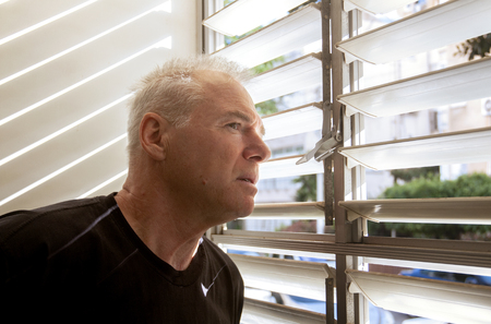man stares out the window through the blindsの写真素材