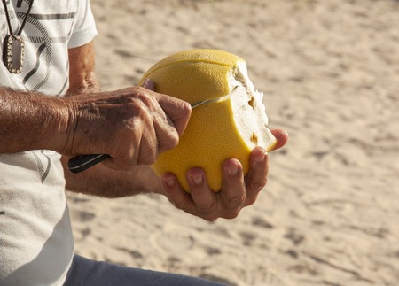 Hands man's cleansing the pomelo from the peel with a knife Shot close-up The background is blurred
