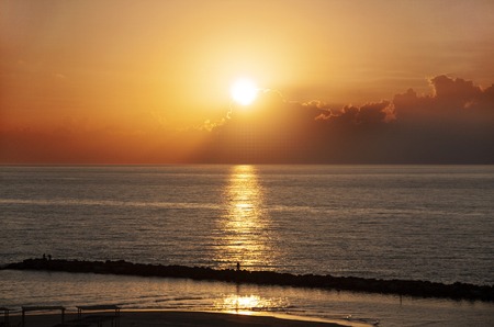 illuminated clouds by the setting sun, which is reflected in the dark sea waterの写真素材