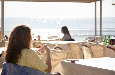 Beautiful woman sitting in a outdoor cafe at a beach resortの写真素材