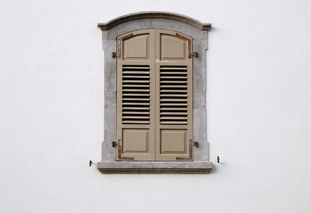 arched window with wooden shutters in a concrete frame on a white wallの写真素材
