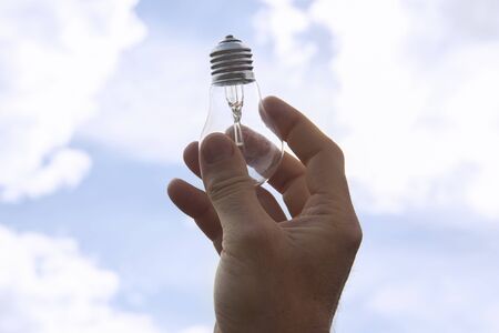 hand with a light bulb on the sky background