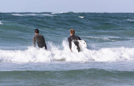 Surfers with a surfboards enter the water