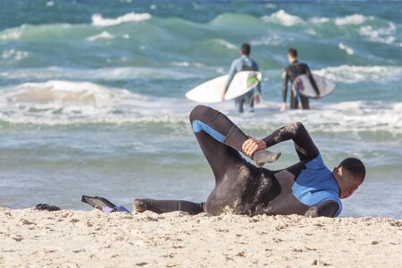 A surfer does a warm-up on the background of the sea on a sandy beachの写真素材