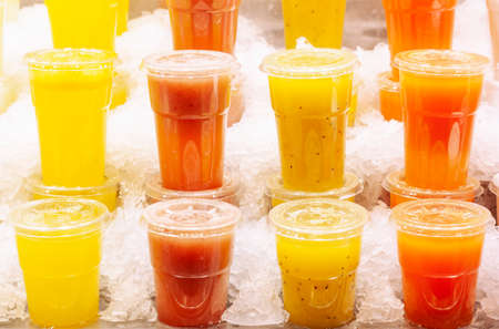 Rows of smoothies made from various tropical fruits stand in ice on the market counterの写真素材