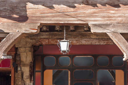 The lantern hangs in the arched wooden open doorway of the gallery of a tudor house in Languedoc
