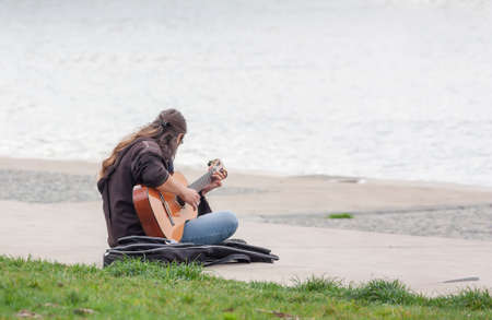 A street musician playing the guitar sitting on the embankment
