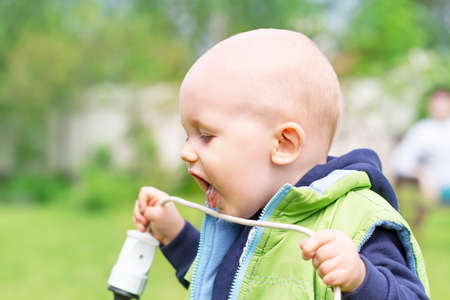 A child pulls an electric wire into his mouth while playing outsideの写真素材