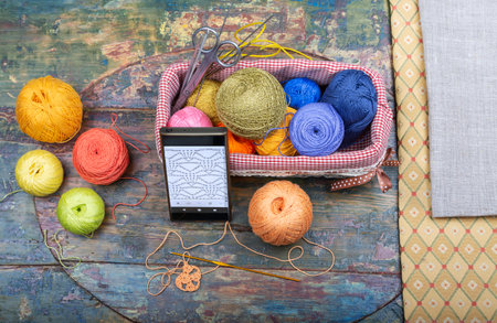 A crochet set and a smartphone are layout on a shabby wooden tableの写真素材