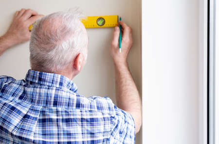 An elderly man measures a wall with a construction level