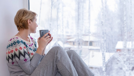 A woman sitting on the windowsill with a cup of tea in winterの写真素材