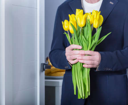 An elder man in a blue suit with yellow tulips in his handsの写真素材