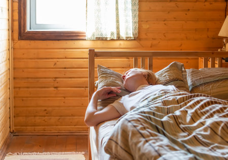 A woman sleeps in a bed in a wooden house illuminated by morning light from windowの写真素材